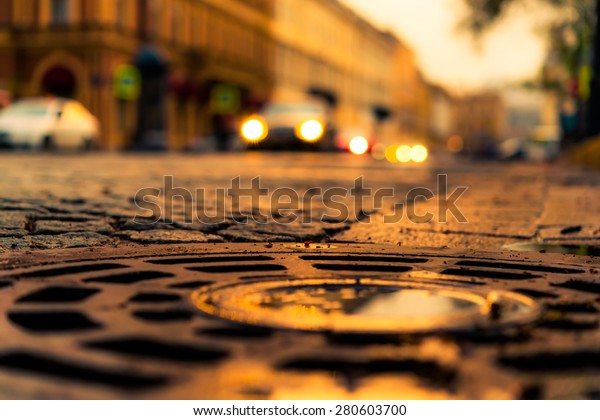 City central square paved with stone, cars\
traveling on the street. View from the hatch on the pavement level,\
image in the yellow toning