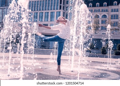 City fountains. Nice young woman feeling the freshness of water while dancing in the fountain