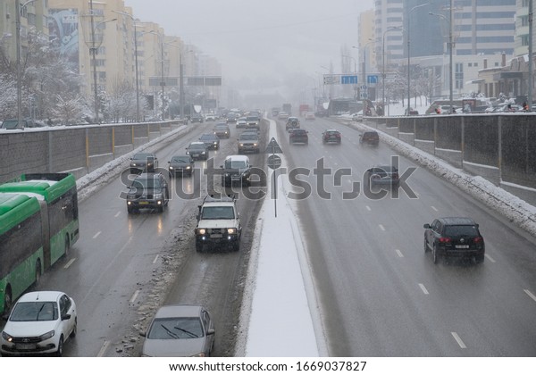 City highway in snowfall with cars and bus on\
it. Urban winter landscape. Frost storm, snowfall, ice. 18.02.2020\
Almaty, Kazakhstan.