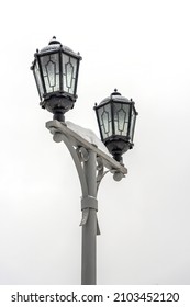 A city lamppost covered with white snow. Vintage lanterns on a light background. Lamppost in the park in winter.