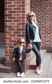 City Life Portrait And Family Fashion Look Of Young Happy Mother And Little Daughter In Leather Jacket. Full Body Family Beautiful Cool Mom And Cute Daughter Near Brick Wall