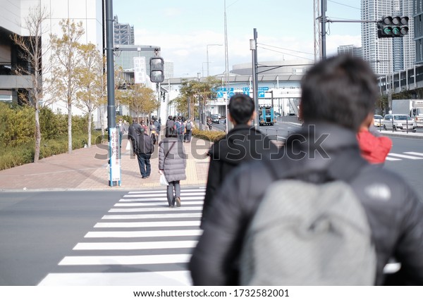 City life in Tokyo, Japan with people walking on\
footpath and japanese language signpost on top is ( bicycle,\
pedestrian defined ) and below street sign is ( Motorcycle down and\
cross please )