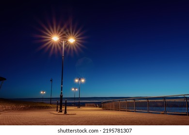 City lights illuminate empty promenade with metal fence and seats. Warm and cold color tone. Nobody. Urban walking area. Night shot. - Powered by Shutterstock