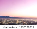 The city lights of the skyline of the Inland Empire near Los Angeles California begin to appear as the sun sets in a dramatic pink sunset. View from Potato Mountain in Claremont Wilderness Park