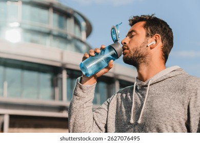 City, man and drinking water with earphones in urban side for fitness and exercise in summer. Female athlete and bodybuilder in day for wellness or rest with podcast or radio during running jogging