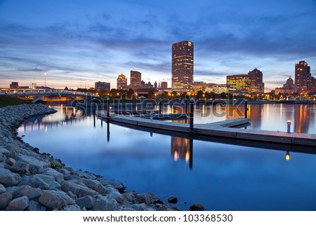 City of Milwaukee skyline. Image of the Milwaukee skyline at twilight with city reflection in lake Michigan and harbor pier.