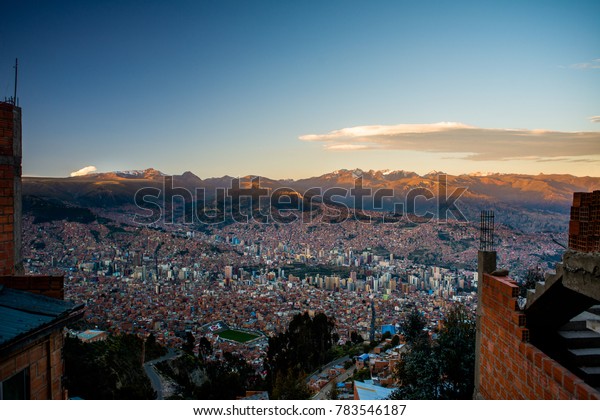 City and\
mountain sunset view of La Paz, the city in Bolivia. A viewpoint\
mirador at the 16 de Julio Mi Teleférico station. Cable cars and\
houses among the mountains ranges.\
