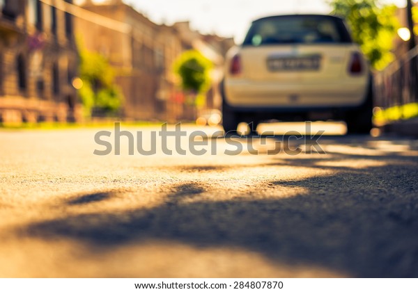 City on a sunny day, a quiet street with trees and\
parking car. View from the level of asphalt, image in the\
yellow-blue toning