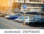 City parking lot with row of parked cars and paid parking sign on pole, parking problems and the role of paid parking zones in urban management.