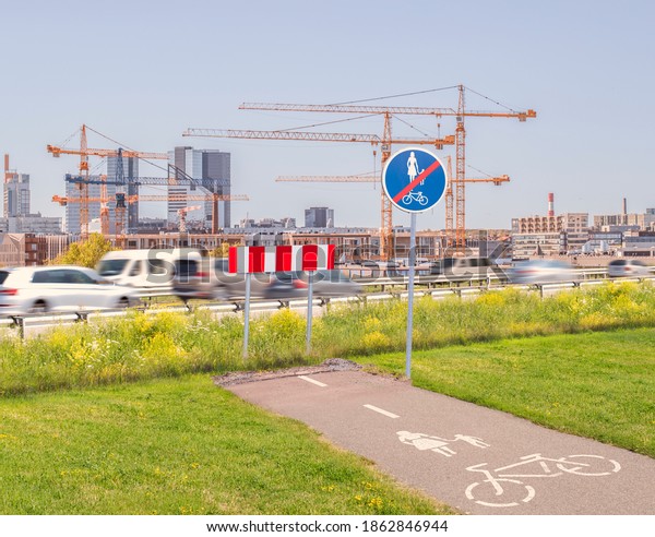 The city planning dilemma - a highway with heavy\
traffic cutting a bicycle and pedestrian path way into a dead end\
with a modern city and skycrapers being constructed in the\
backround by cranes