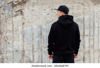 City portrait of handsome guy wearing black blank hoodie or sweatshirt and baseball cap with space for your logo or design. Mockup for print
