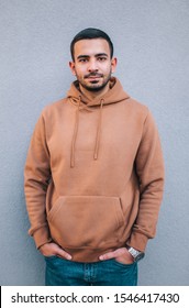 City Portrait Of Handsome Hipster Guy With Beard Wearing Brown Blank Hoodie Or Hoody With Space For Your Logo Or Design. Mockup For Print