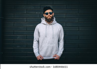 City Portrait Of Handsome Hipster Guy With Beard Wearing Gray Blank Hoodie Or Hoody With Space For Your Logo Or Design And Casual Beanie. Mockup For Print