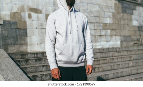 City Portrait Of Handsome Hipster Guy With Beard Wearing Gray Blank Hoodie Or Hoody With Space For Your Logo Or Design. Mockup For Print