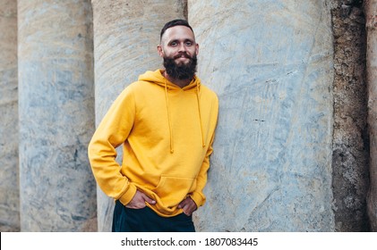 City Portrait Of Handsome Hipster Guy With Beard Wearing Yellow Blank Hoodie Or Sweatshirt With Space For Your Logo Or Design. Mockup For Print