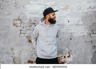 City portrait of handsome hipster guy with beard wearing gray blank hoodie and baseball cap with space for your logo or design. Mockup for print - Powered by Shutterstock