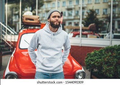 City portrait of handsome hipster man with beard wearing gray blank hoodie or sweatshirt and hat with space for your logo or design. Mockup for print