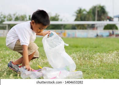 At The City Public Park. Asian Child Boy Is A Volunteer For Clean Up The Field Floor. He Picking Up Many Plastic Bottle And Straw On The Ground. Save Environmental And Reduce Waste Concept.