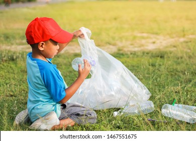 At The City Public Park. Asian Child Boy Is A Volunteer For Clean Up The Field Floor. He Picking Up Many Plastic Bottle And Straw On The Ground. Save Environmental And Reduce Waste Concept.