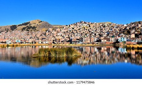 City of Puno reflected in Tranquil waters of lake Titicaca. Puno - capital city of the Puno Region - important regional center and major tourist destination in Peru. Photo taken 2018-08-27.