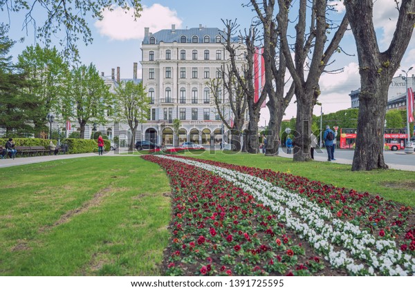 City Riga, Latvia Republic. Latvian flag from\
flowers, red and white. Tourists walk on street and cars drive. May\
7. 2019 Travel photo.