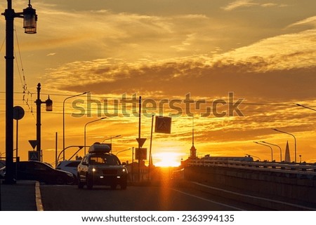 City roads with silhouettes of cars at sunset, backlit. Colorful yellow sky with clouds over the city.