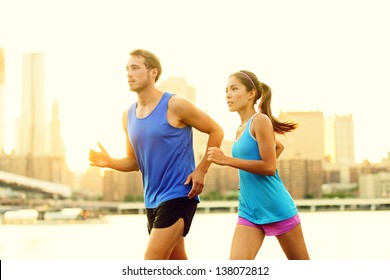 City Running Couple Jogging Outside. Runners Training Outdoors Working Out In Brooklyn With Manhattan, New York City In The Background. Fit Multiracial Fitness Couple, Asian Woman, Caucasian Man.