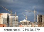 A city skyline with a few cranes in the background. The sky is cloudy and the mood of the image is somewhat gloomy