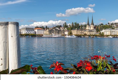 City Skyline. Scenic View Of Lake Lucerne, Churche (Hofkirche), Hotels, Old Town Buildings, Cruise Ships And Pedalos. Foreground With Red Flowers And Boat Anchor Pillars. Lucerne, Switzerland. 