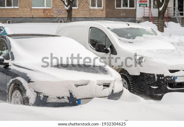 City street after blizzard. Stuck cars under the\
snow and ice. Buried vehicle in snowdrift on the road. Parking lots\
in winter after heavy snowfall. Uncleaned roads. Record-breaking\
amounts of snow.