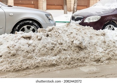 City street driveway parking lot with many cars covered by snow stucked after heavy blizzard snowfall on winter day by dirty snowy pile. Snowdrifts and freezed vehicles. Extreme weather conditions