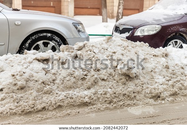 City street driveway parking lot with many\
cars covered by snow stucked after heavy blizzard snowfall on\
winter day by dirty snowy pile. Snowdrifts and freezed vehicles.\
Extreme weather conditions