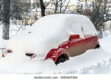 City Street Driveway Parking Lot Spot With Small Car Covered Snow Stuck Trapped After Heavy Blizzard Snowfall Winter Day By Big Snowy Pile. Snowdrifts And Freezed Vehicles. Extreme Weather Conditions