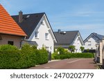 City street of single-family modern houses Germany against blue sky. German suburban small town residential area with row eco sustainable life building neighborhood suburb. Urban car parking driveway.