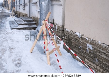 City streets after snowfall. Snow-covered sidewalks are fenced off with warning tape on wooden pyramids. Melting snow on water pipes freezes into ice and icicles that are dangerous for pedestrians