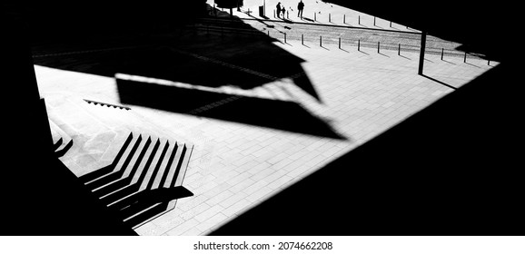 City Wide Square, Empty Public Space With Stairs In Architectural Shades And Lights, And Silhouette Of People Standing In The Distance, In Black And White From Above 