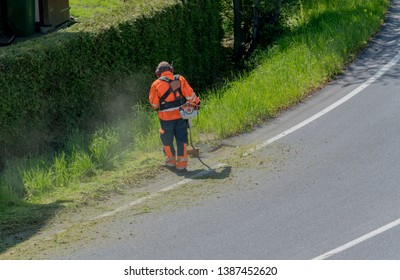 A City Worker Clearing The Roadside Of Grass And Weeds With A Weed Eater