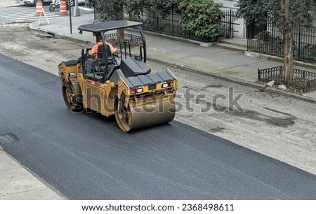 city worker paves road with paving vehicle (new asphalt installation on urban street) tandem vibratory roller 
