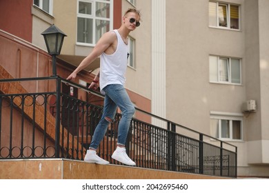 City Youth Concept. Boy Dreaming Of Freedom Hanging In Air One Arm And One Leg. Young Man In The City On The Buildings Background.