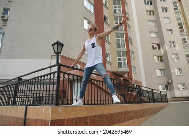 City Youth Concept. Boy Dreaming Of Freedom Hanging In Air One Arm And One Leg. Young Man In The City On The Buildings Background.