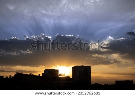 Cityline near sunset with sun shining behind buildings through dark inky clouds