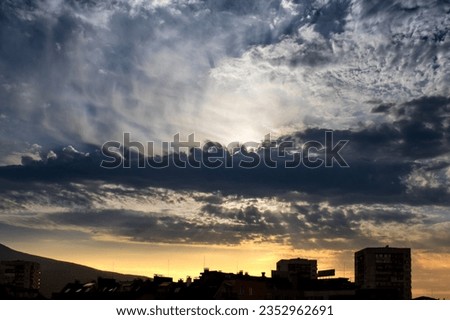 Cityline near sunset with sunrays showing through dark inky clouds