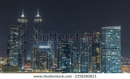 Cityscape with illuminated skyscrapers of Dubai Business Bay and water canal aerial night timelapse. Modern skyline of residential and office towers on waterfront. Cranes working on construction site