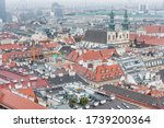 Cityscape with red tiles rooftops and tower of Jesuit Church of the old town of Vienna in a heavy snowy day. View at the tower of St. Stephen