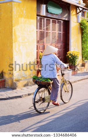 Cityscape with senior woman riding bicycle on street in Old city of Hoi An in Southasia in Vietnam. Elderly lady in Vietnamese hat on bike in Hoian.