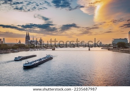 Cityscape view of the city of Koln, the Rhine River, bridges and various barges and ships during majestic sunset.