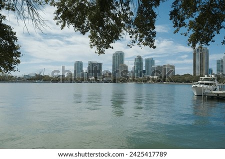 Cityscape of water with tall buildings on a sunny day with boats in the foreground. With a blue sky on a sunny day at the Vinoy  Basin waterfront in St. Petersburg, Florida. Trees in foreground top.