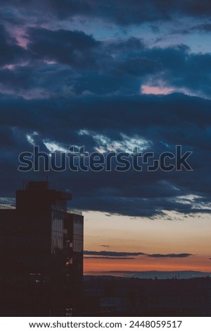 Cityscape with wonderful varicolored vivid dawn. Amazing dramatic multicolored cloudy sky above dark silhouettes of city buildings. Atmospheric background of sunrise in overcast weather.