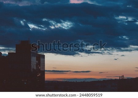 Cityscape with wonderful varicolored vivid dawn. Amazing dramatic multicolored cloudy sky above dark silhouettes of city buildings. Atmospheric background of sunrise in overcast weather.