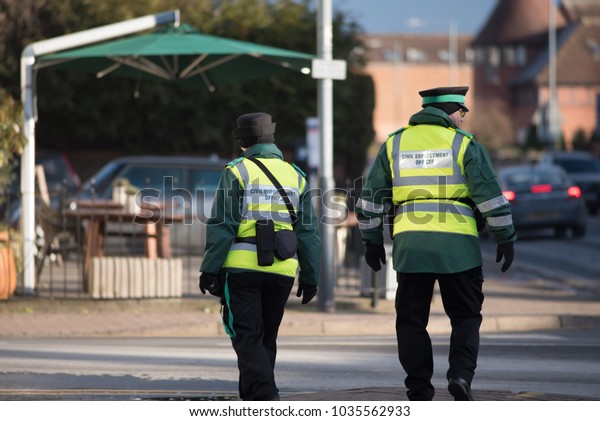 civil enforcement wardens\
walking down street together with traffic and pub garden in\
background